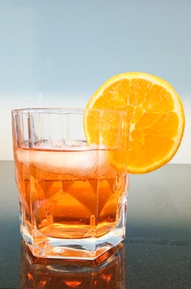 A cocktail glass with orange liquid and and a slice of orange.